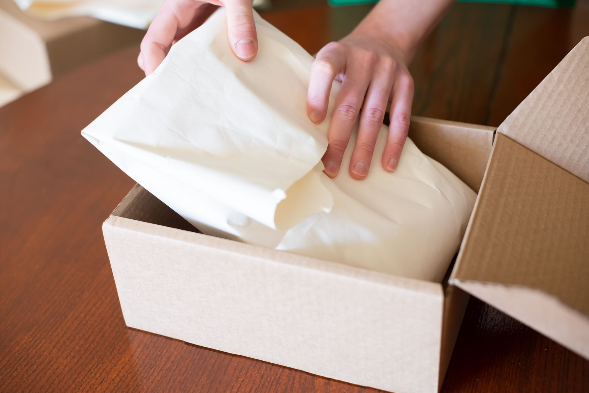 Hands placing a tissue-wrapped order into a cardboard box